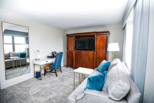 A hotel room with a sofa, a desk, a chair, a wardrobe, and a television.
