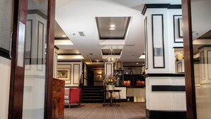 Un hall d’hôtel avec un comptoir d’accueil, un escalier et un lustre.