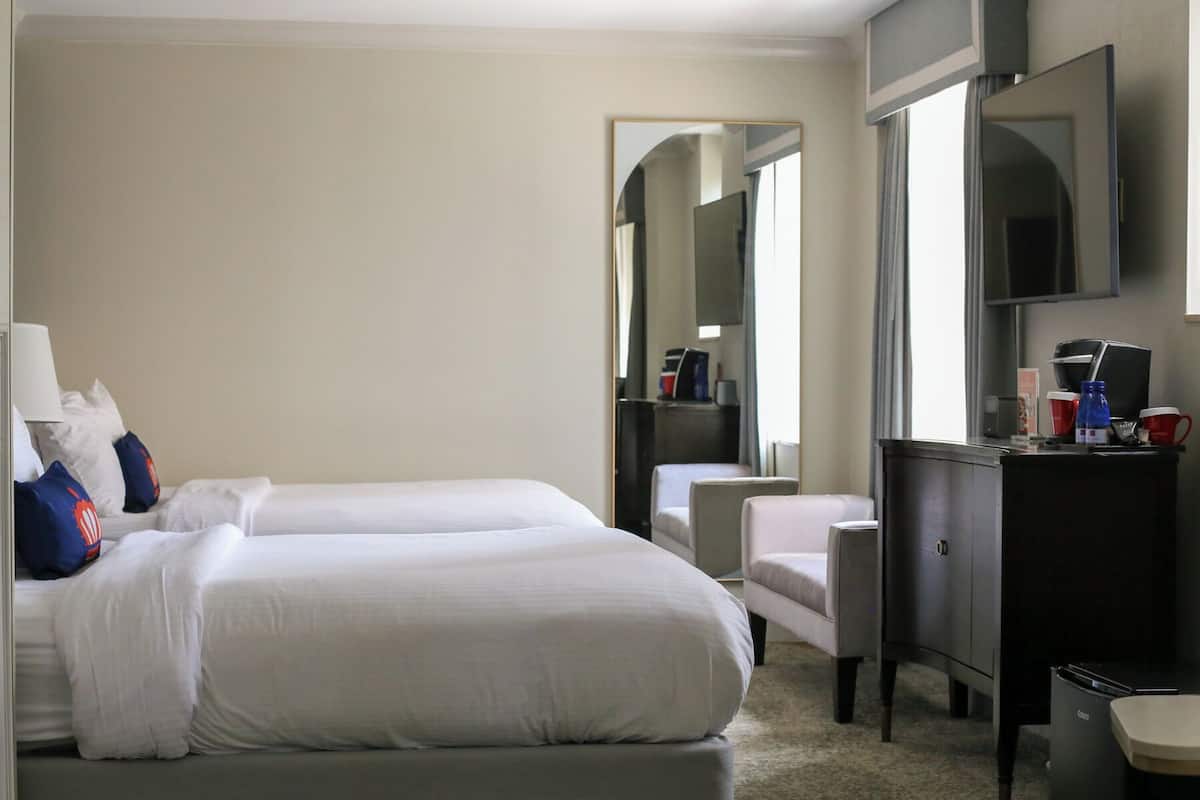 A hotel room with two beds, a desk, a chair, a mirror, and a television.