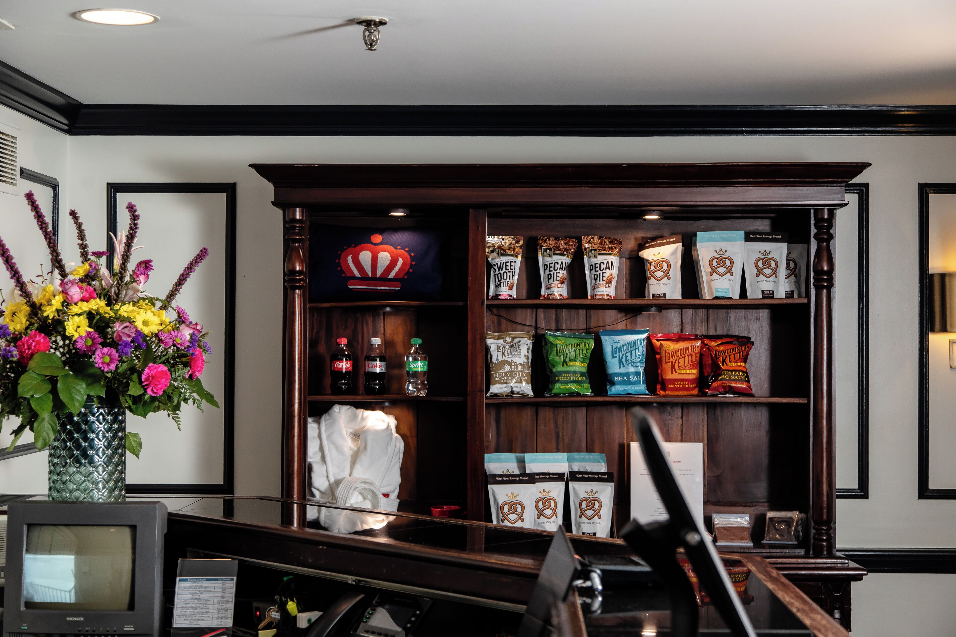 A room with a wooden shelf displaying various packaged goods, a vase with colorful flowers, and a television.