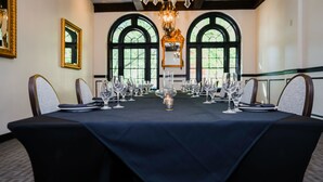 Une salle de conférence avec une longue table préparée pour une réunion, de grandes fenêtres et un lustre.