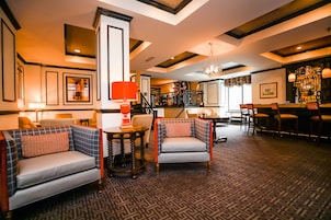 Eine Hotellobby mit Barbereich, Sitzgelegenheiten und einer Treppe zu einer oberen Etage.