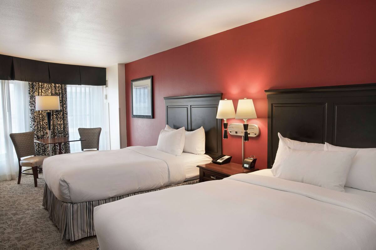 A hotel room with two beds, a desk with chairs, and a nightstand with lamps.