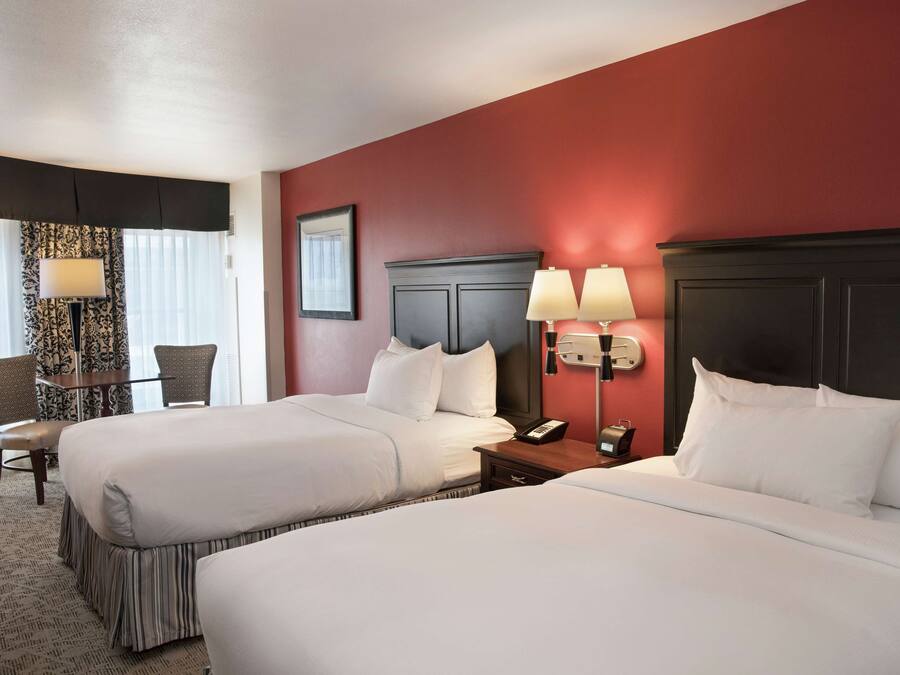 A hotel room with two beds, a desk with chairs, and a nightstand with lamps.