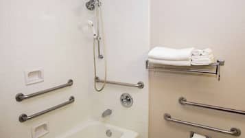 A bathroom with a bathtub, a shower, and handrails. There are also towel racks and a toilet paper holder.