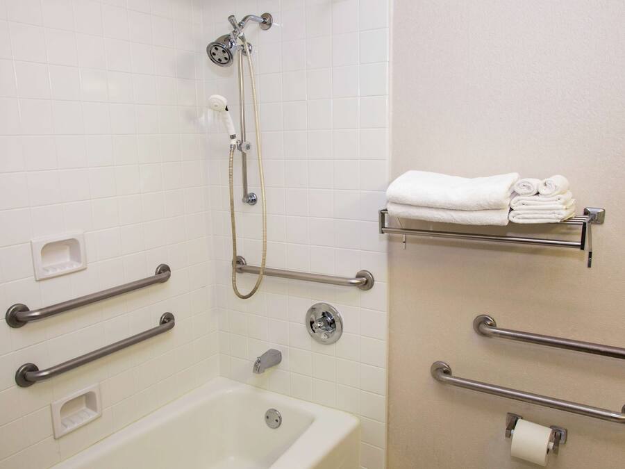A bathroom with a bathtub, a shower, and handrails. There are also towel racks and a toilet paper holder.