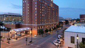 A multi-story hotel with a prominent corner building, a covered entrance, and a parking area with several cars.