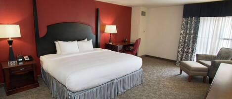 Habitación de hotel con una cama grande, dos mesitas de noche con lámparas, un escritorio, una silla y una ventana con cortinas.