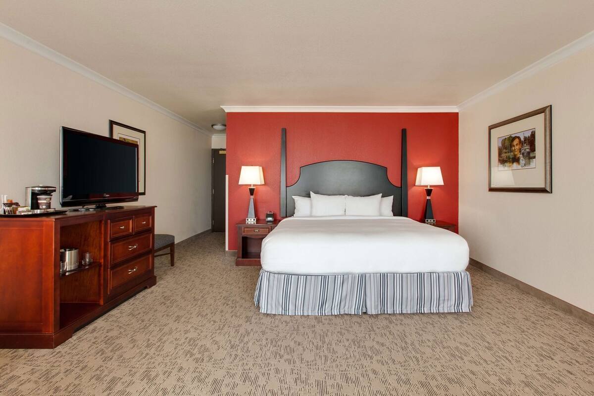 A hotel room with a bed, a TV, a dresser, and two bedside lamps.