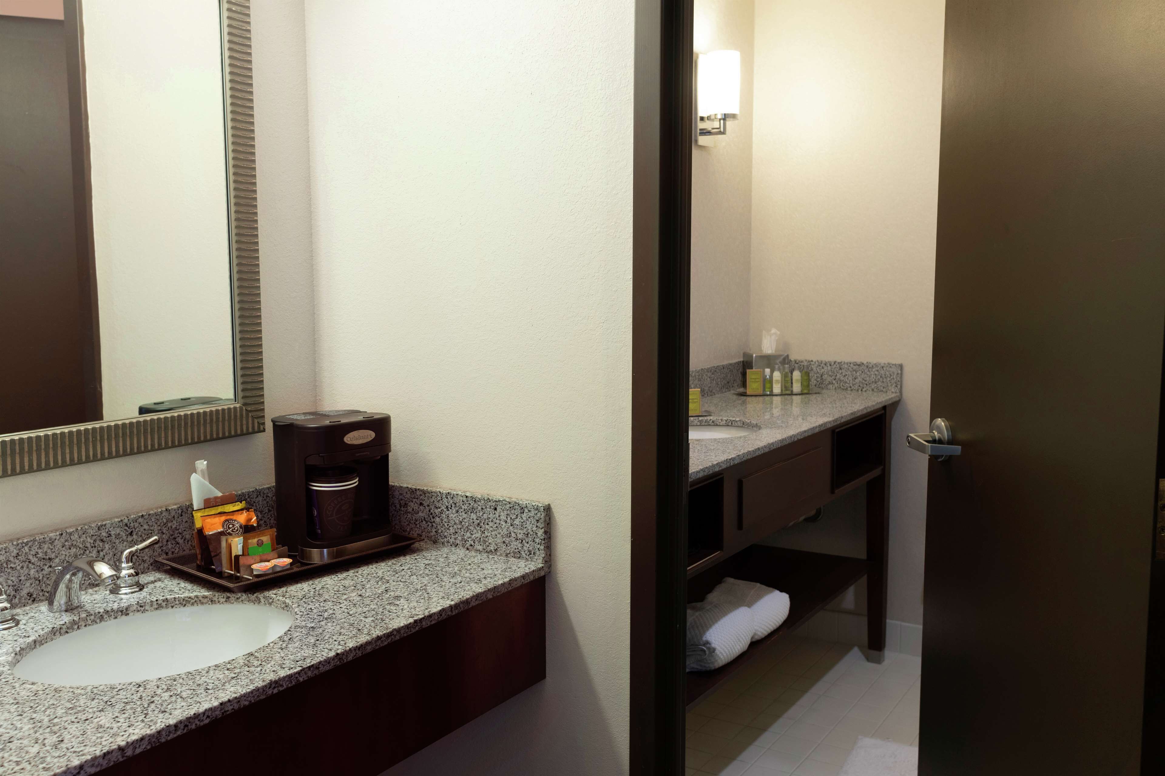 A hotel bathroom with a granite countertop sink, a coffee maker, and a mirror.
