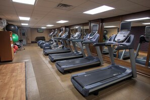 Une salle de sport équipée de plusieurs tapis de course, de ballons d’exercice et d’un mur entièrement recouvert de miroirs.