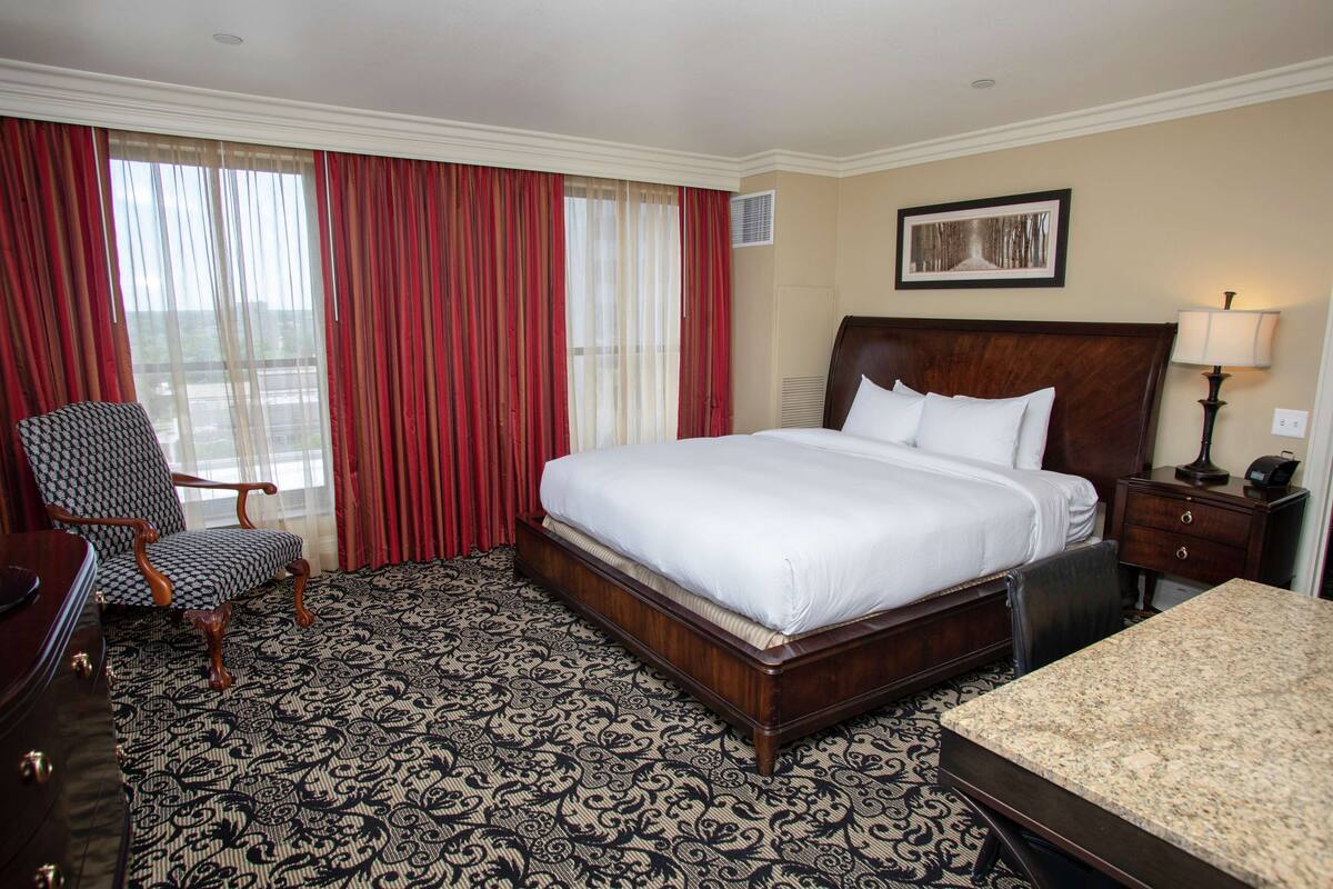 A hotel room with a large bed, a chair, a desk, and a window with curtains.
