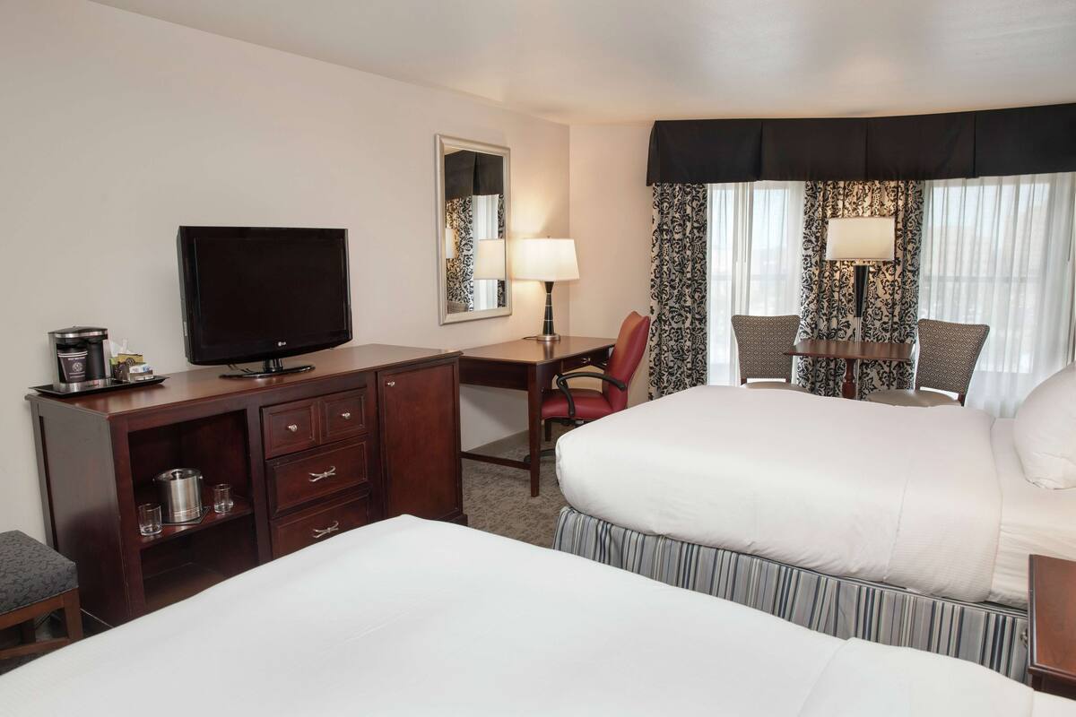 A hotel room with two beds, a desk with a TV, a chair, and a lamp.