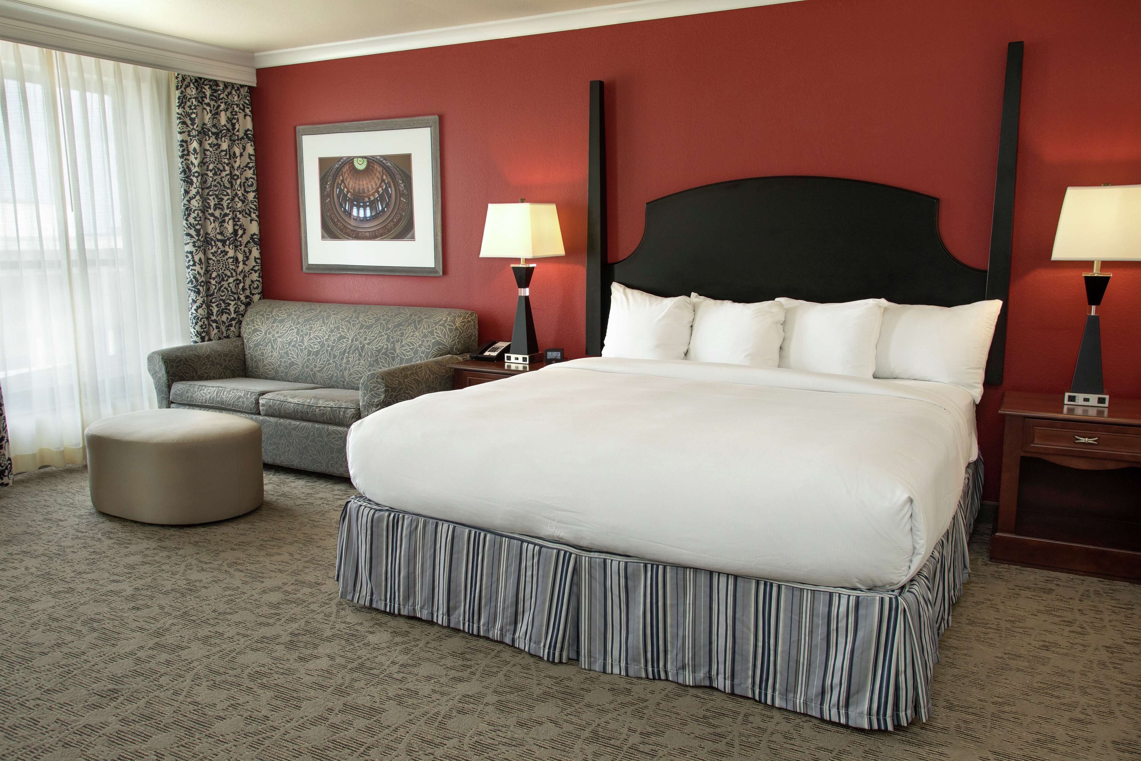 A hotel room with a large bed, a sofa, a chair, and a small table.