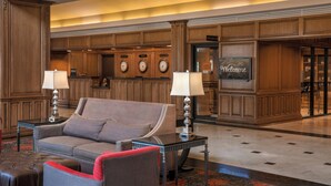 A lobby with a grey sofa, two side tables with lamps, a red throw pillow, and a 'Welcome' sign.