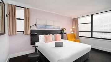 A hotel room with a large bed, a desk, a chair, and a window with a city view.