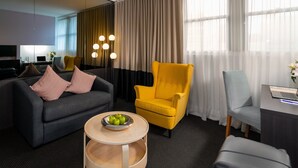 A modern hotel room with a grey sofa, yellow armchair, and a small round table with apples. - Park Regis City Centre (Sydney)