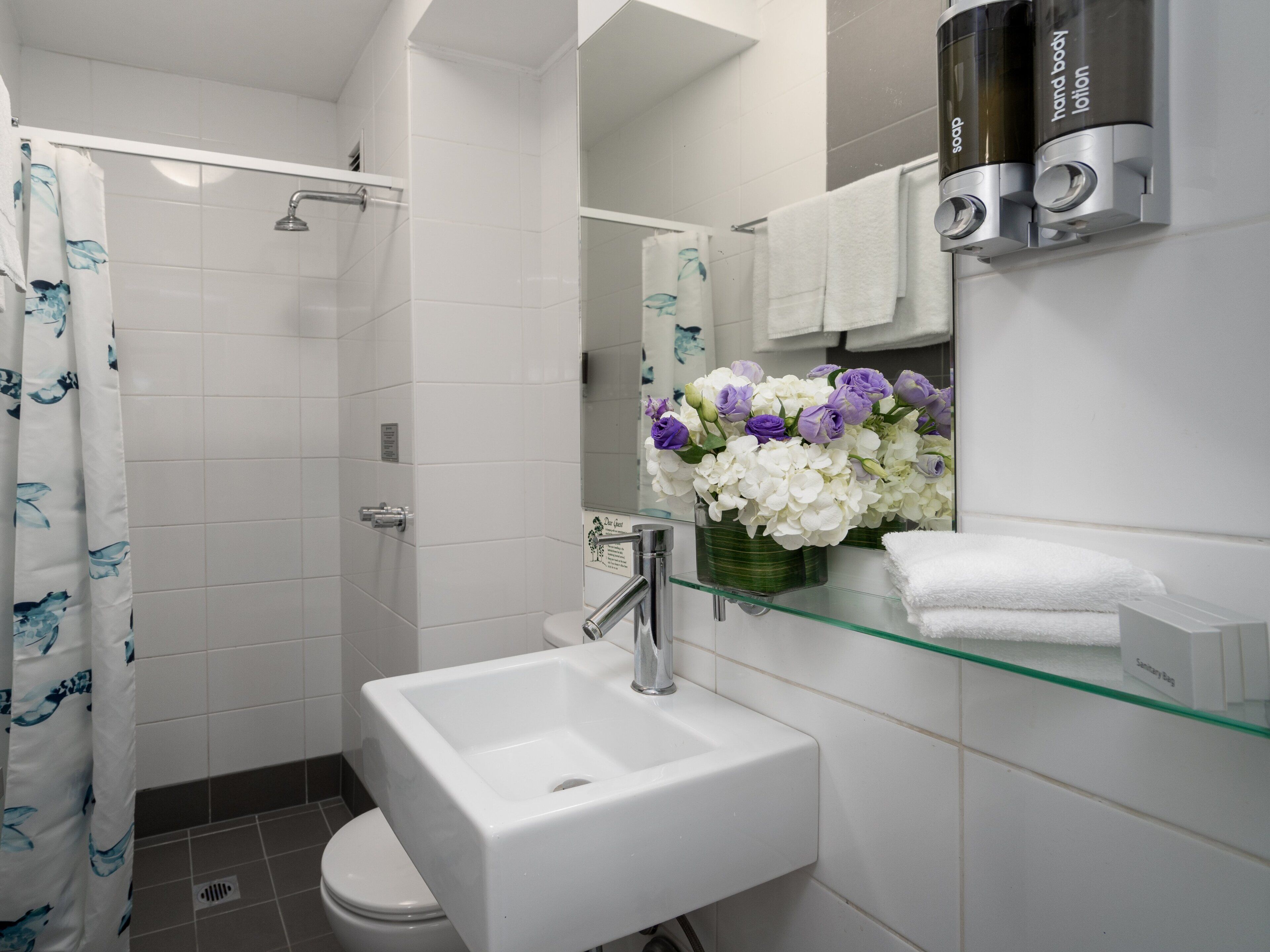 A modern bathroom with a glass sink, a shower, and a toilet.