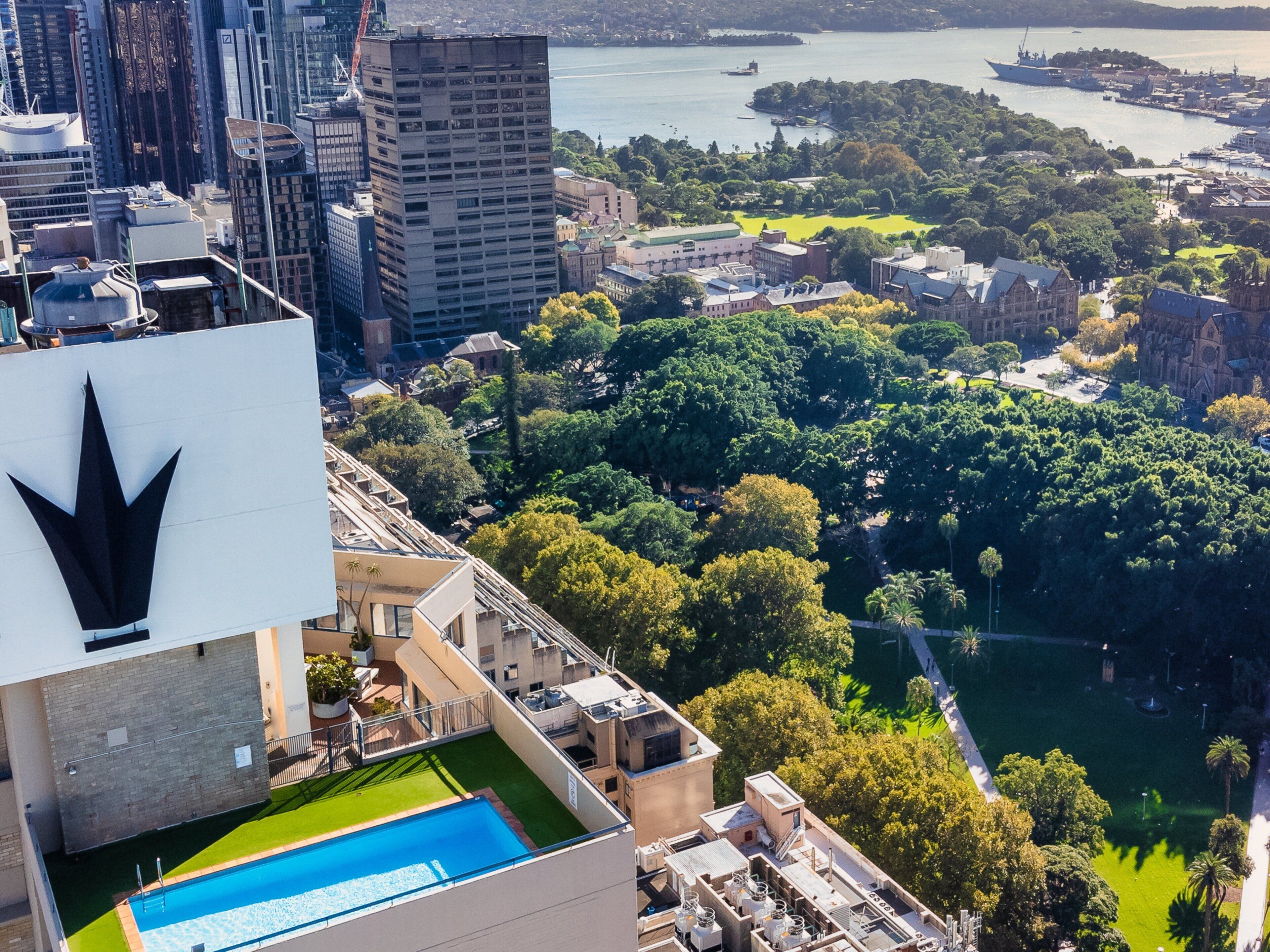 Un immeuble de grande hauteur doté d’une piscine sur le toit et offrant une vue sur le paysage urbain, avec une rivière et des espaces verts.