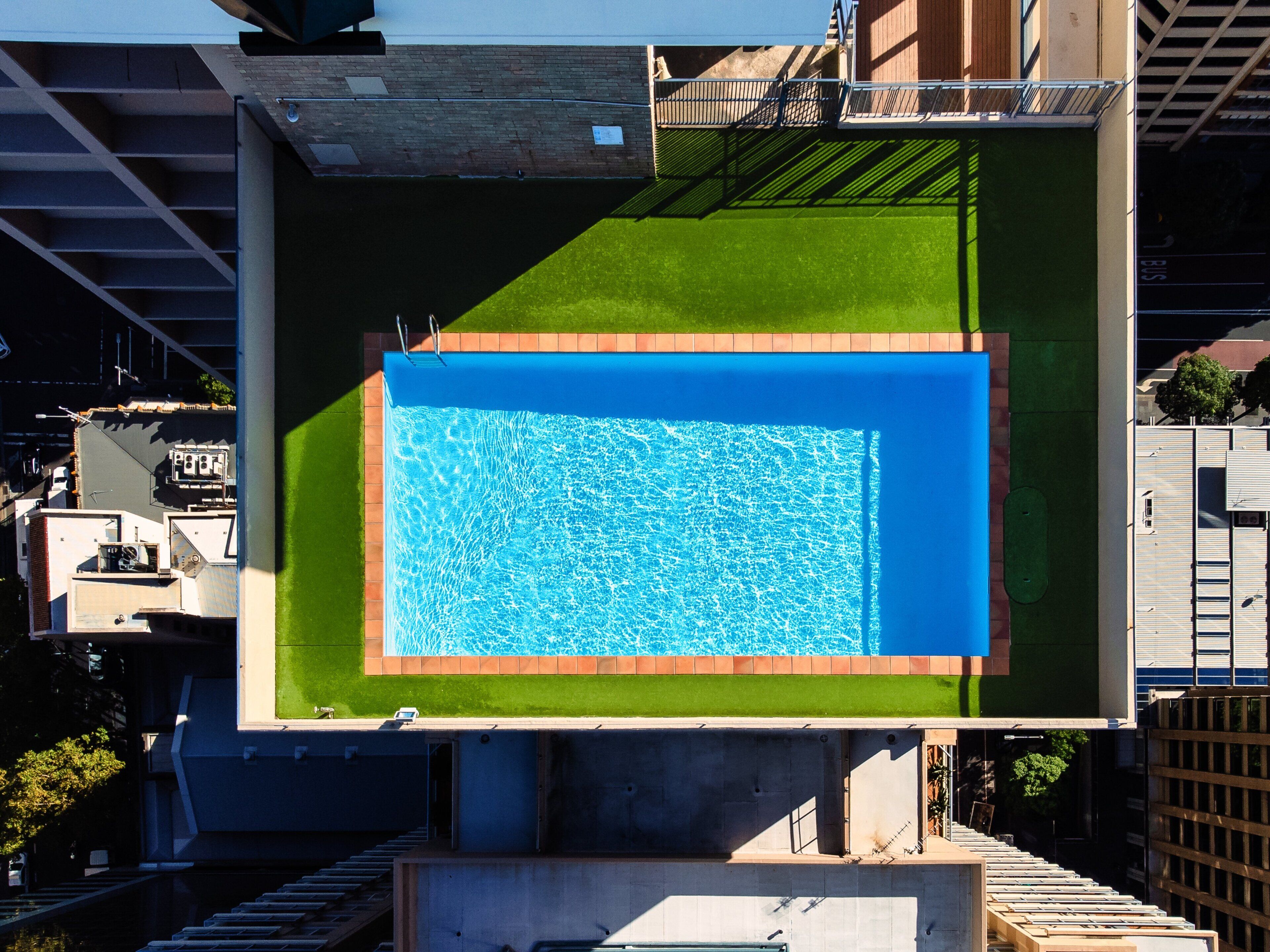 A rooftop swimming pool with a clear blue water surface, surrounded by a green lawn and a brick border.