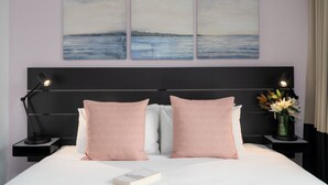 A neatly made bed with pink checkered pillows, a bedside lamp, and a book on the nightstand. - Park Regis City Centre (Sydney)