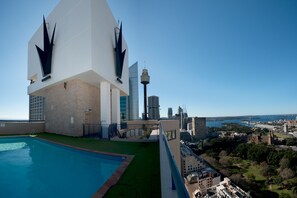 Una piscina en la azotea con vistas despejadas de un horizonte urbano, que incluye una torre destacada y un edificio histórico.