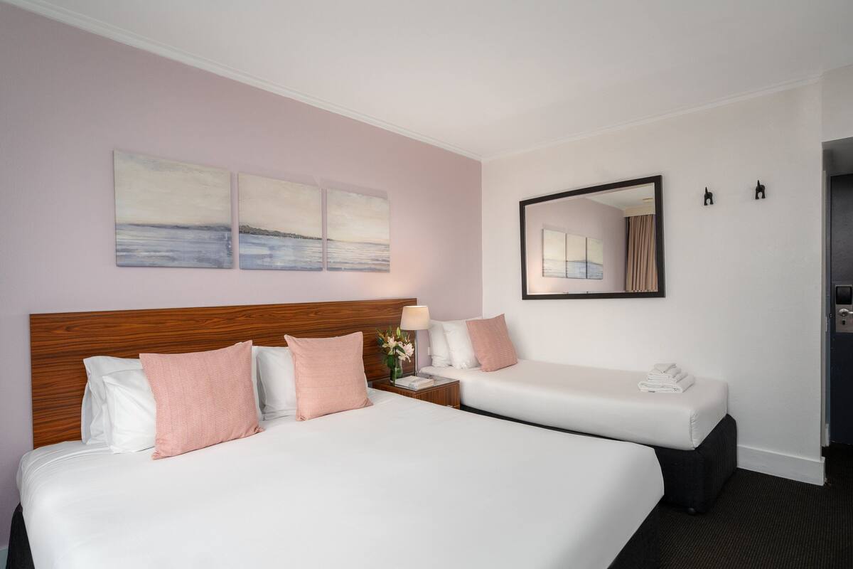 A hotel room with two beds, a wooden headboard, a nightstand with a lamp, and artwork on the wall.