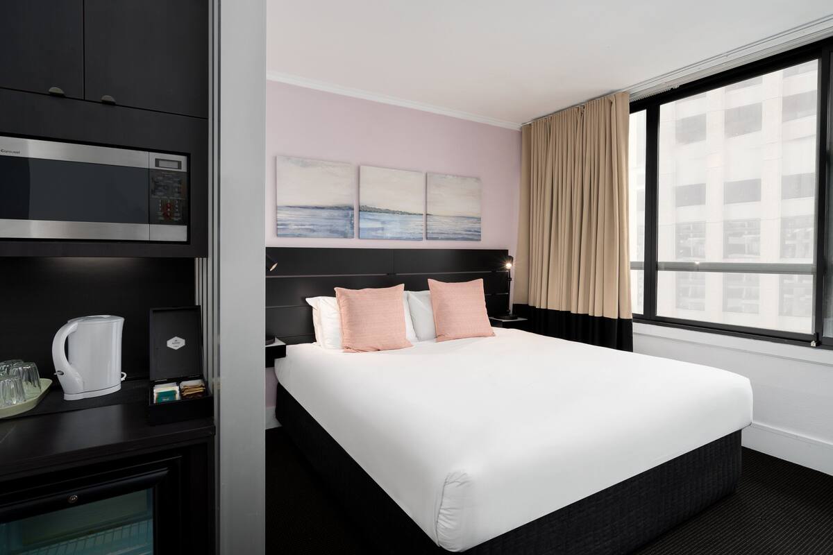 A hotel room with a bed, a minibar, a coffee machine, and a window with curtains.