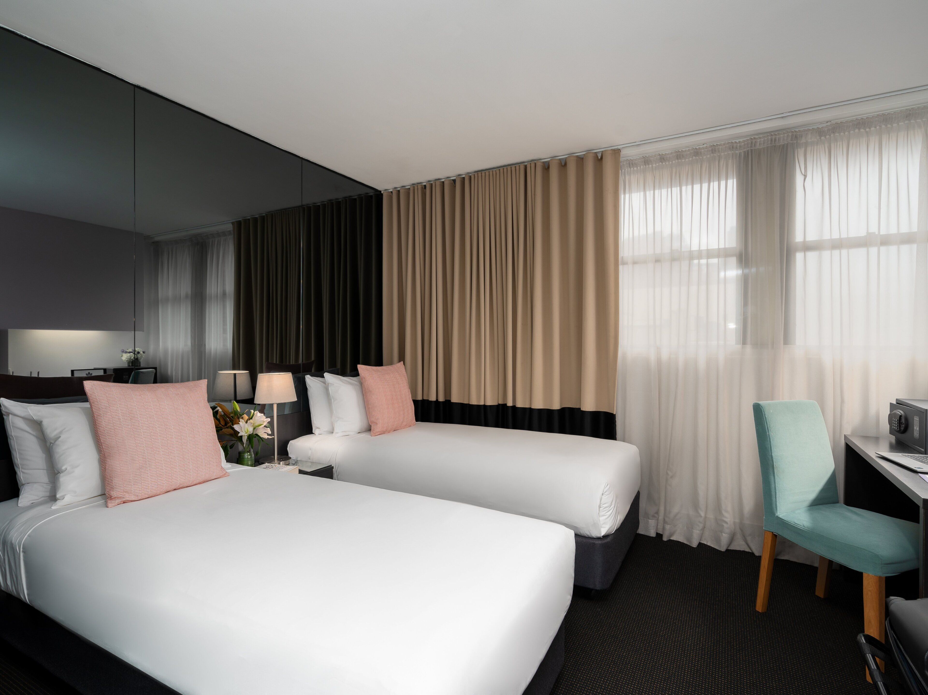 A hotel room with two beds, a desk, a chair, and a large window with curtains.