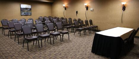 A conference room with rows of chairs, a long table, and wall-mounted lighting.