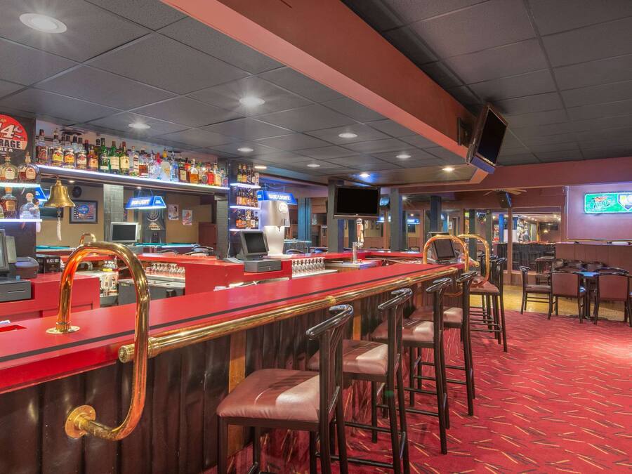 Un espace bar avec un comptoir rouge, des tabourets et une variété de bouteilles d’alcool.