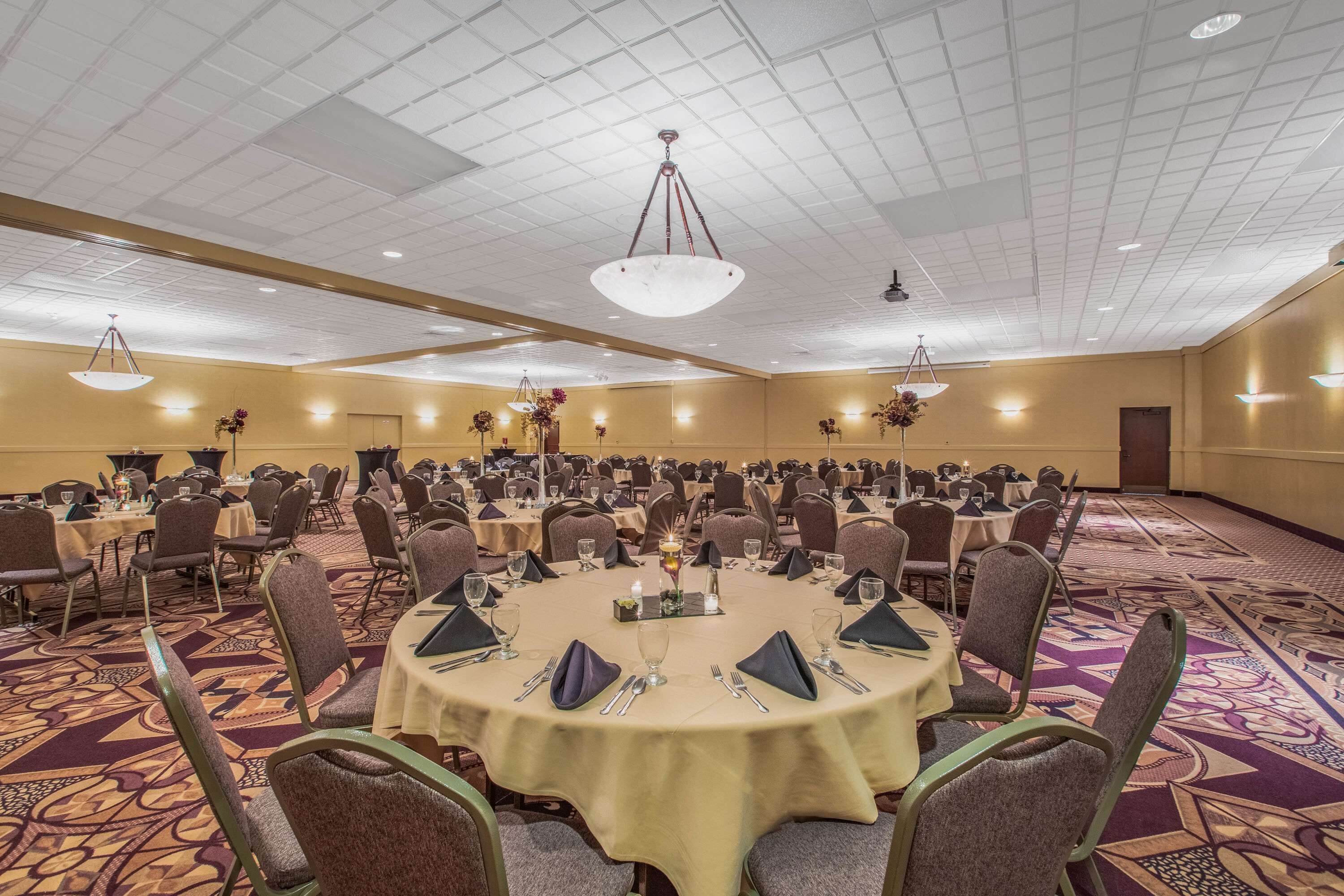 A large banquet hall with round tables, chairs, and chandeliers.