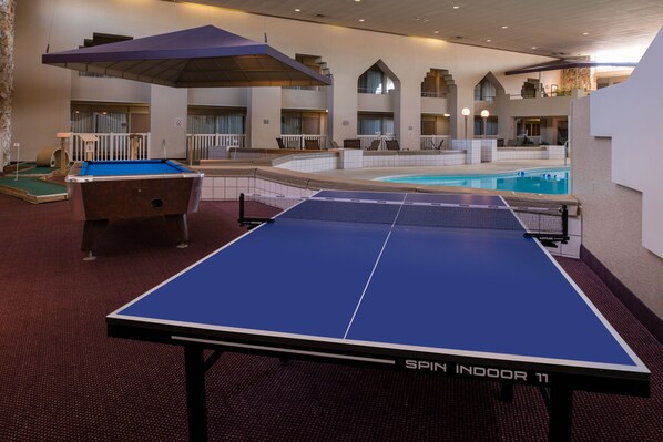 A pool table and a billiards table in a hotel lobby with a pool and a covered seating area.