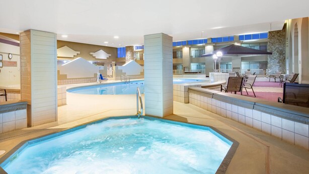 Een hotel lobby met een groot binnenzwembad, een bubbelbad en een zithoek met stoelen en tafels.