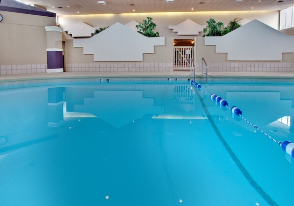 An indoor swimming pool with clear lane markings, a starting block, and a staircase leading to a door.