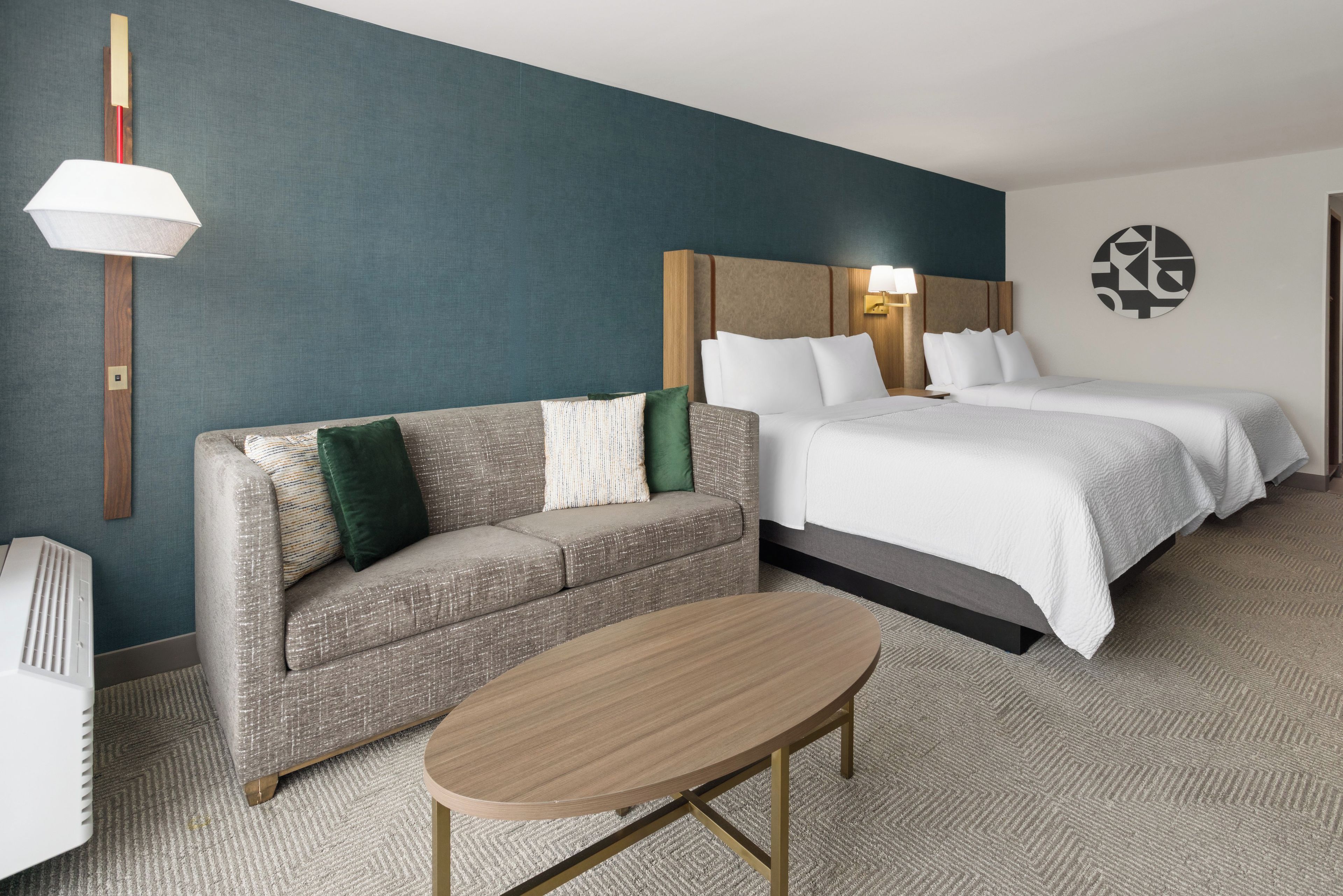 Ein Hotelzimmer mit einer Couch, einem Bett mit zwei Kissen, einem Nachttisch und einer Wandlampe.