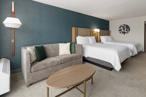 Habitación de hotel con sofá, cama con dos almohadas, mesita de noche y lámpara de pared.
