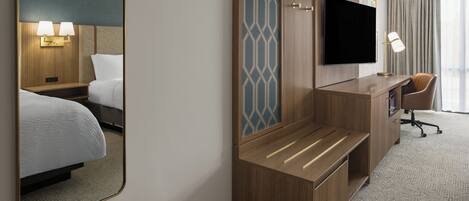 A hotel room with a bed, a desk, a chair, a flat-screen TV, and a mirror.