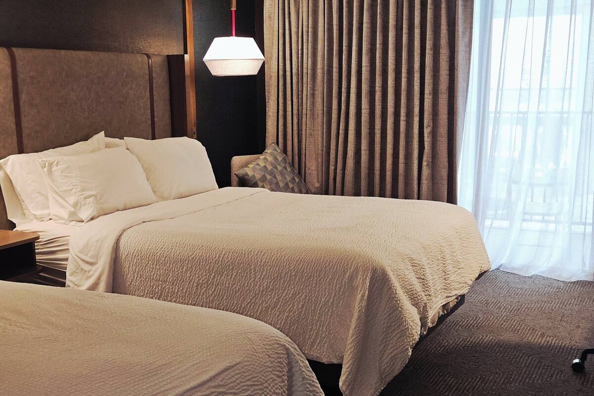 Ein Hotelzimmer mit zwei Betten, einem Nachttisch, einer Lampe und Blick ins Freie.