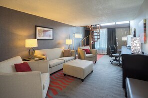 A hotel room with a sofa, ottoman, desk, lamp, and a staircase. - Holiday Inn Harrisburg - Hershey Area, I-81 by IHG (Grantville)
