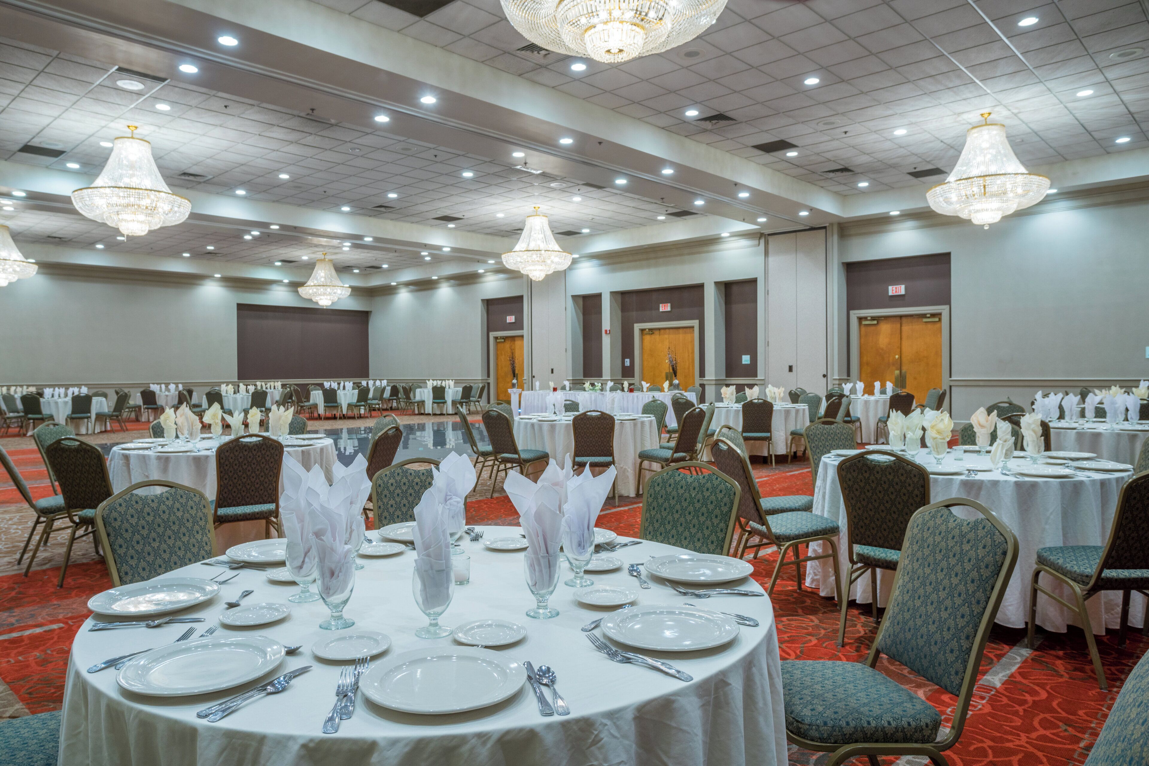 A banquet hall with round tables, chairs, and chandeliers.