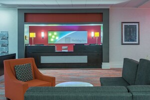 Zona de recepción de hotel con pared roja, un letrero de Holiday Inn, dos lámparas, un cuadro enmarcado y un mostrador de recepción.