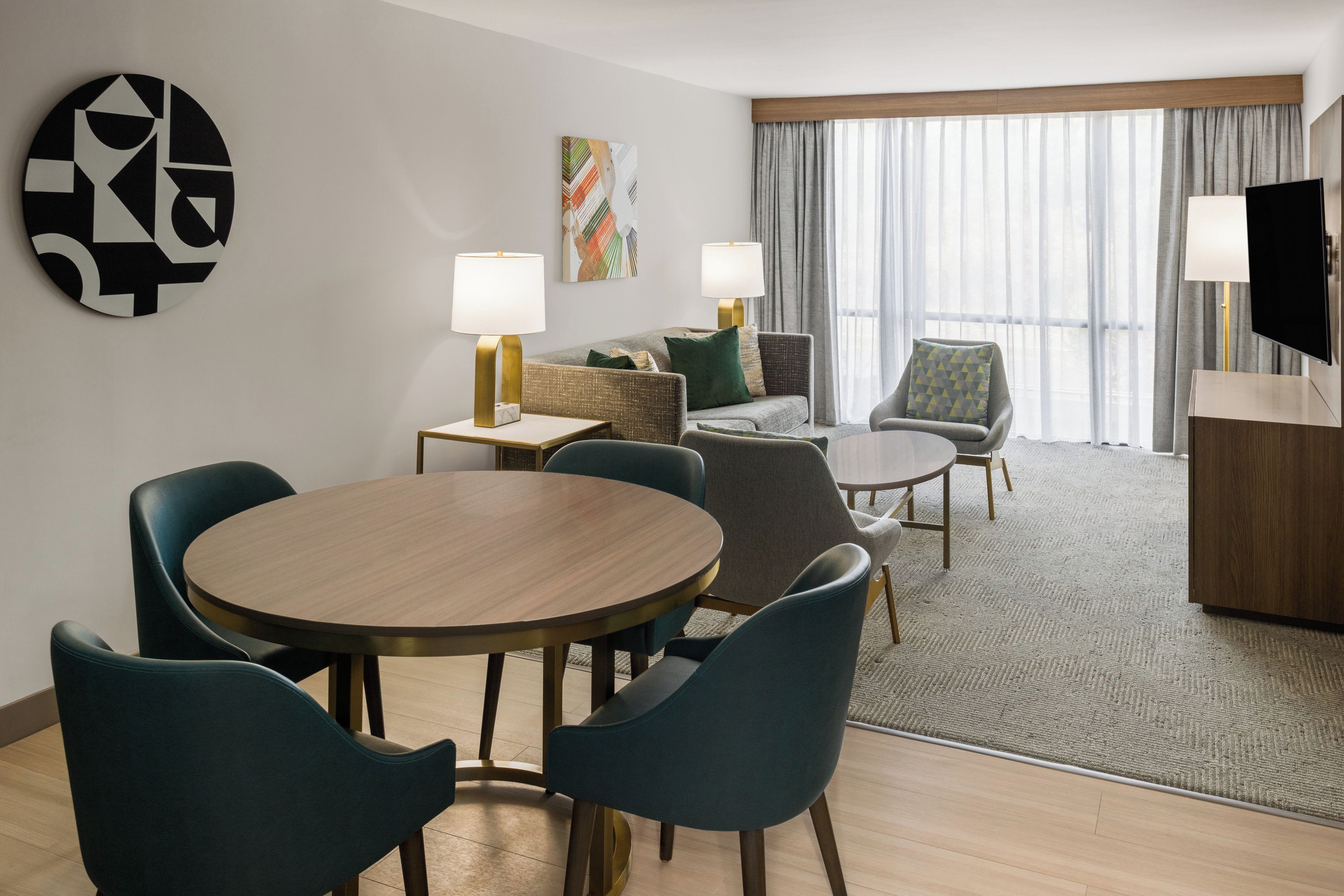 A hotel room with a dining area, a sofa, a TV, and a window with curtains.