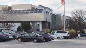 A parking lot with several cars, a modern building with a flat roof, and an American flag.