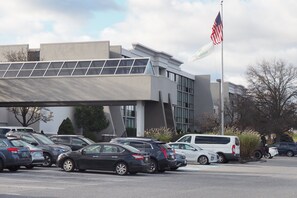 A parking lot with several cars, a modern building with a flat roof, and an American flag. - Holiday Inn Harrisburg - Hershey Area, I-81 by IHG (Grantville)