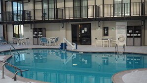 An indoor swimming pool with a clear view of the pool area, including the poolside chairs and the poolside railing.