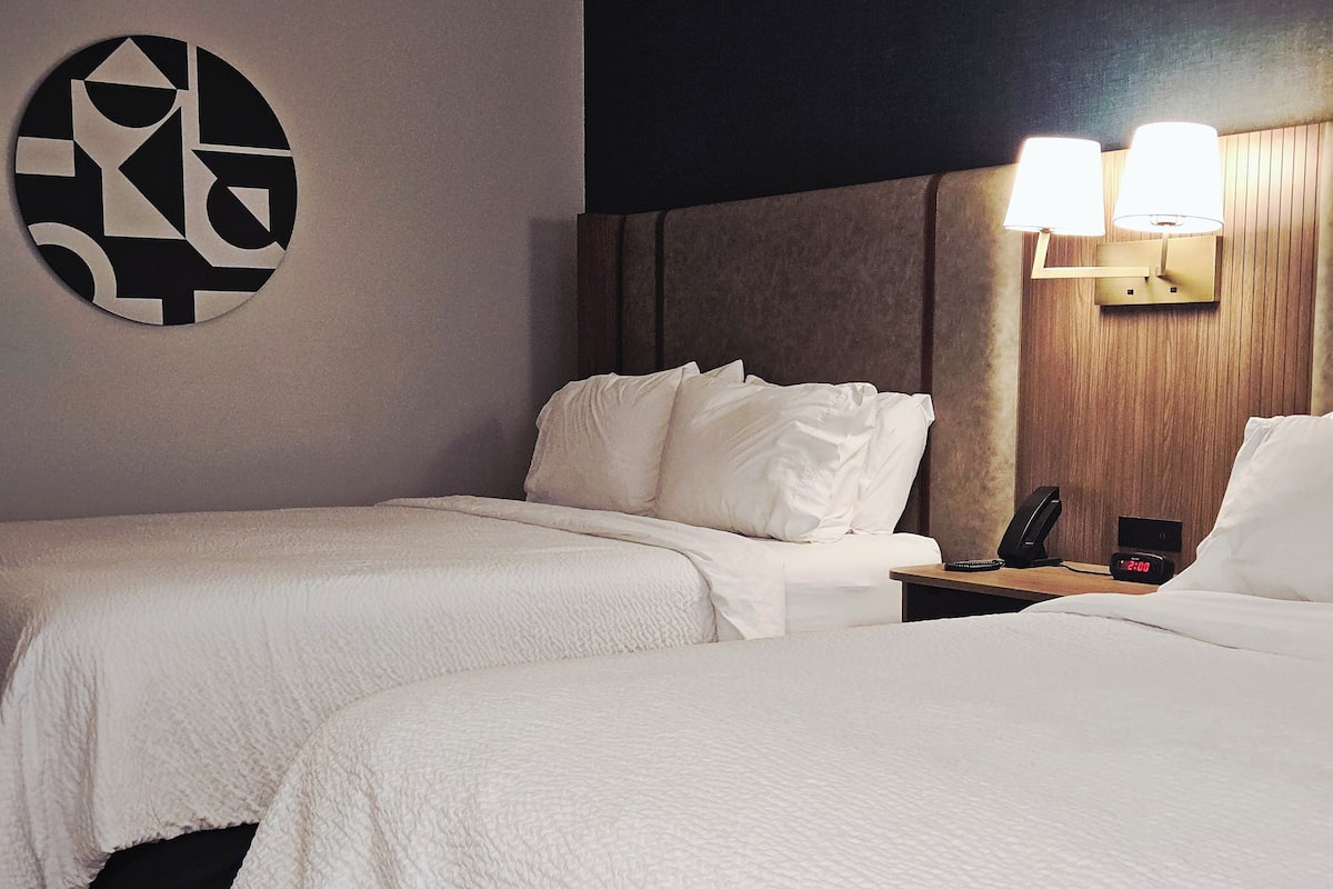 A hotel room with two beds, a wall clock, and a lamp.