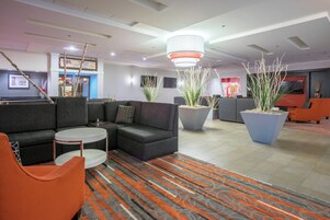A modern lobby with a sectional sofa, a round coffee table, potted plants, and a patterned carpet.
