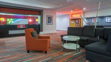 A hotel lobby with a reception desk, seating area, and a sign for a restaurant.