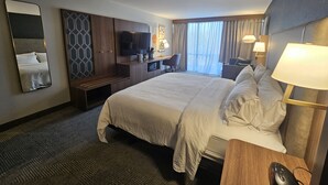 A hotel room with a large bed, a desk, a TV, and a chair.